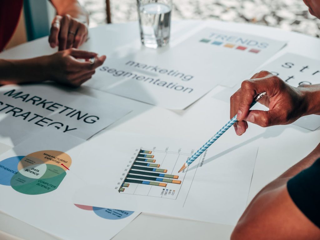a-person-holding-blue-and-white-pencil-7688102 Team working on marketing strategy using data charts and papers in an office meeting.